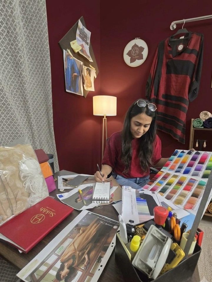 Urvi Sadh at her studio desk among fabric swatches, sketches and a finished piece